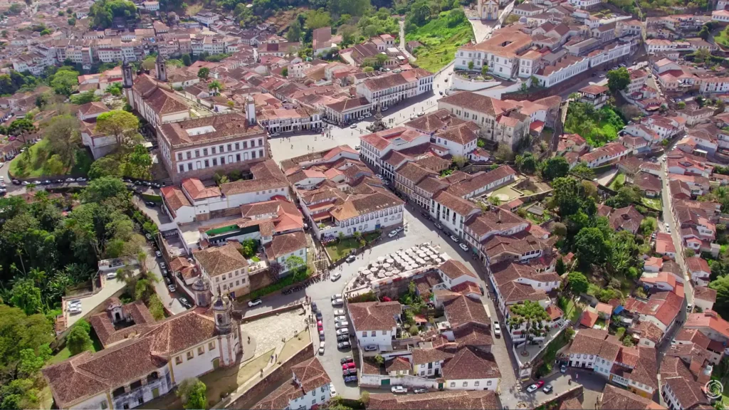 Vista aérea completa da Praça Tiradentes, uma das joias das cidades pitorescas Brasil, mostrando o Museu da Inconfidência, o monumento central e a movimentação de turistas.