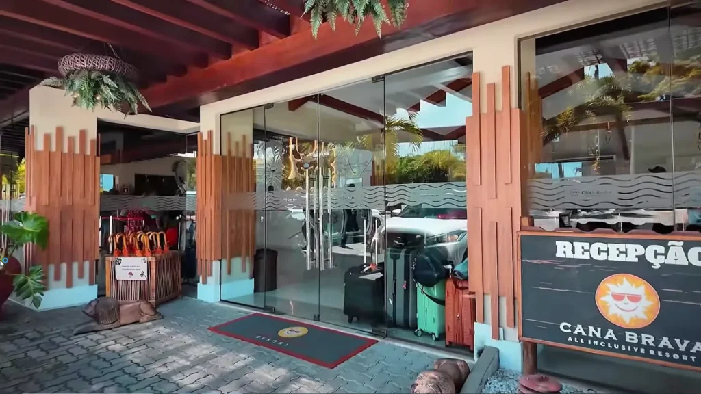 Fachada de vidro da recepção do Cana Brava Resort com malas de viagem e decoração rústica.