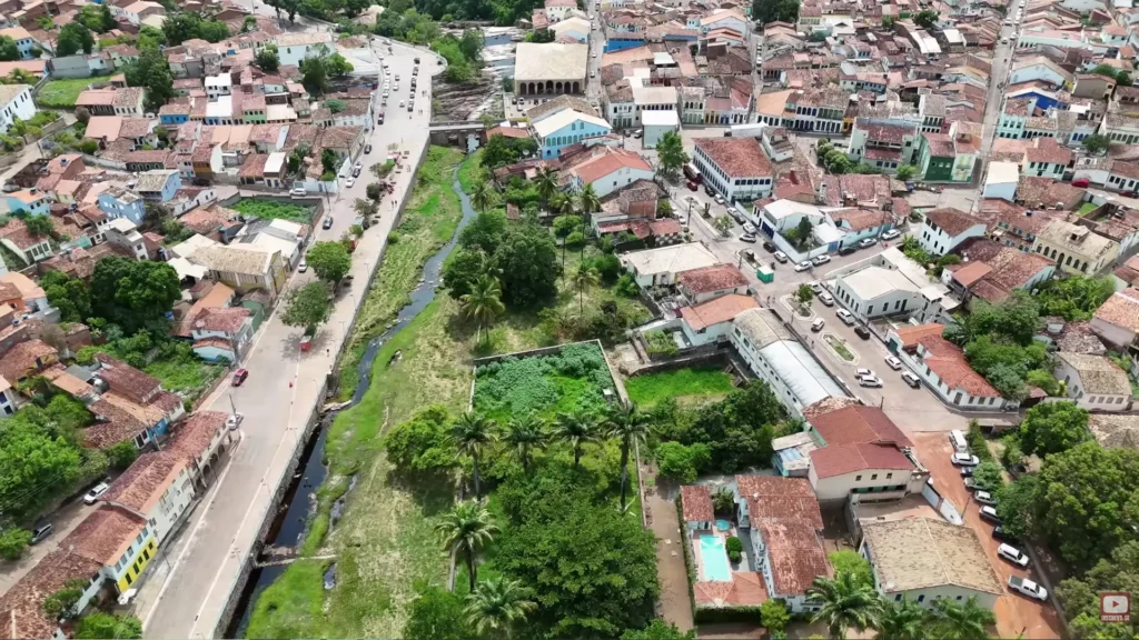 Vista aérea longitudinal seguindo o curso do rio que corta Lençóis, ladeado por vegetação, ruas e casas.