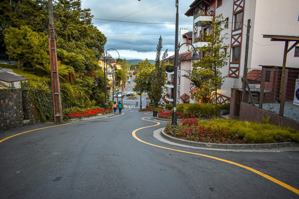 Vista da famosa Rua Torta em Gramado, uma ladeira sinuosa cercada por canteiros de flores vermelhas e prédios com arquitetura em estilo europeu.