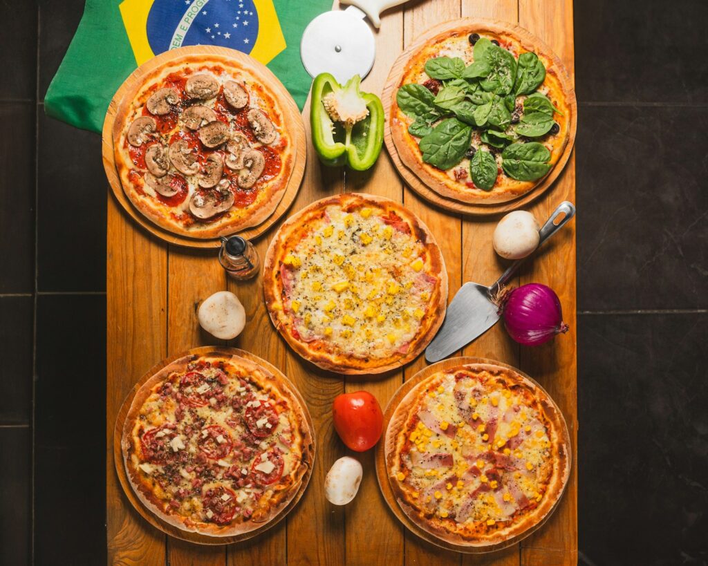 Uma mesa com quatro pizzas ao lado de uma bandeira.