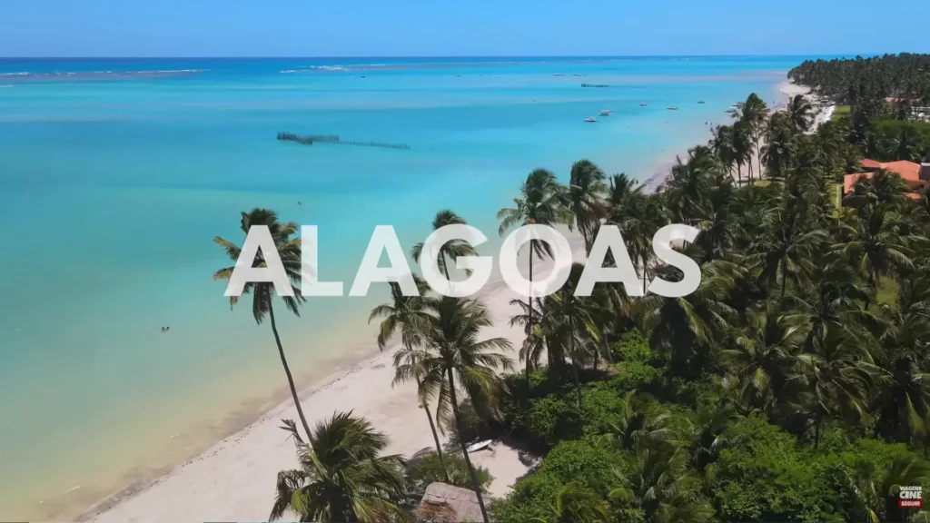 Paisagem de praia tropical com muitos coqueiros, areia branca e o texto ALAGOAS sobreposto em letras brancas grandes.
