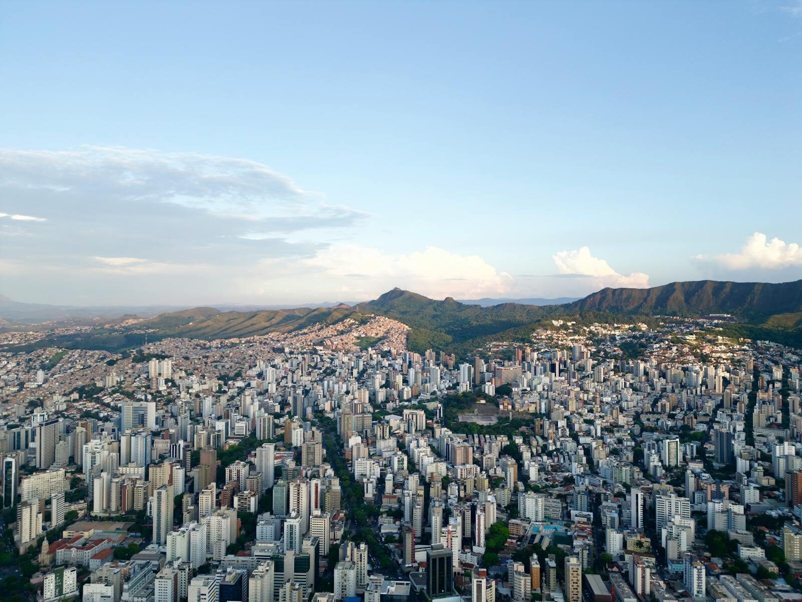 Vista aérea deslumbrante do horizonte de Belo Horizonte com colinas onduladas ao fundo, ao entardecer.