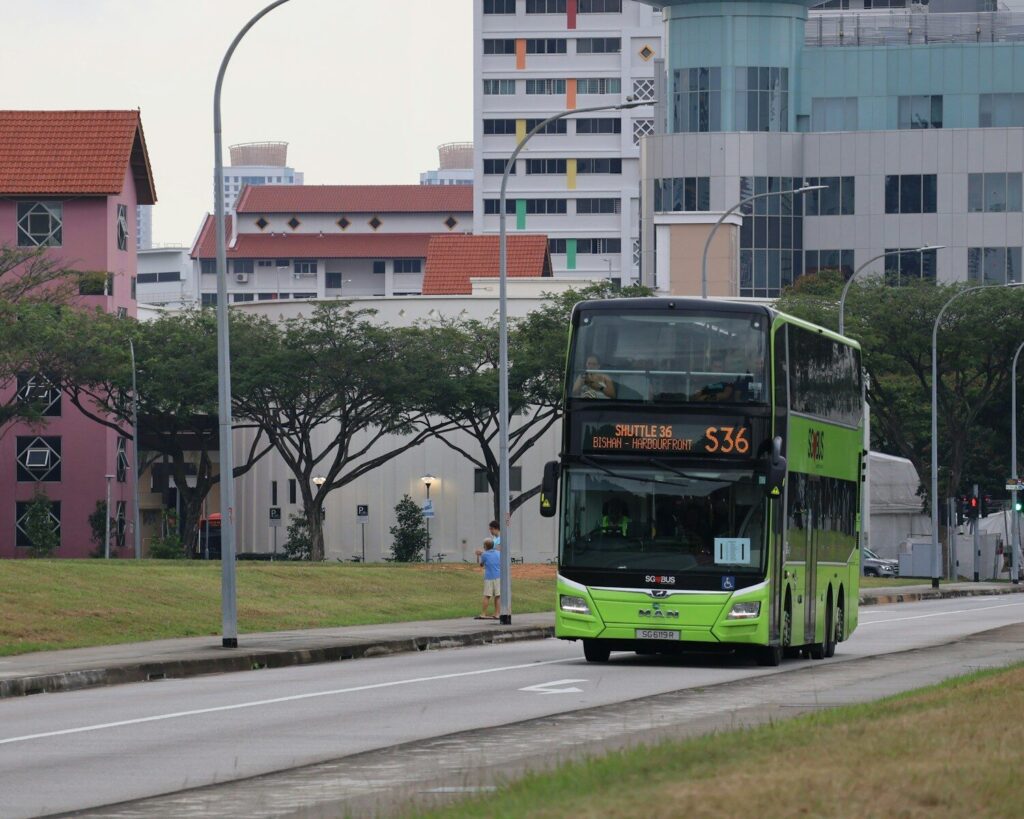 A green double-decker bus drives on the road.