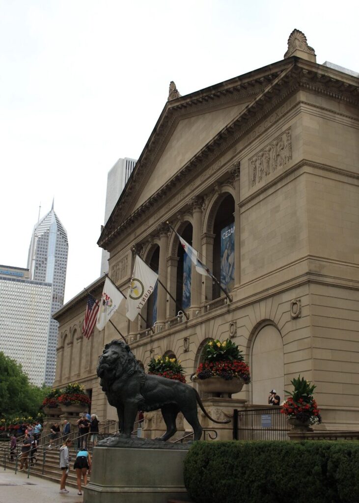 uma estátua de um leão em frente ao Instituto de Arte de Chicago com uma grande torre do relógio