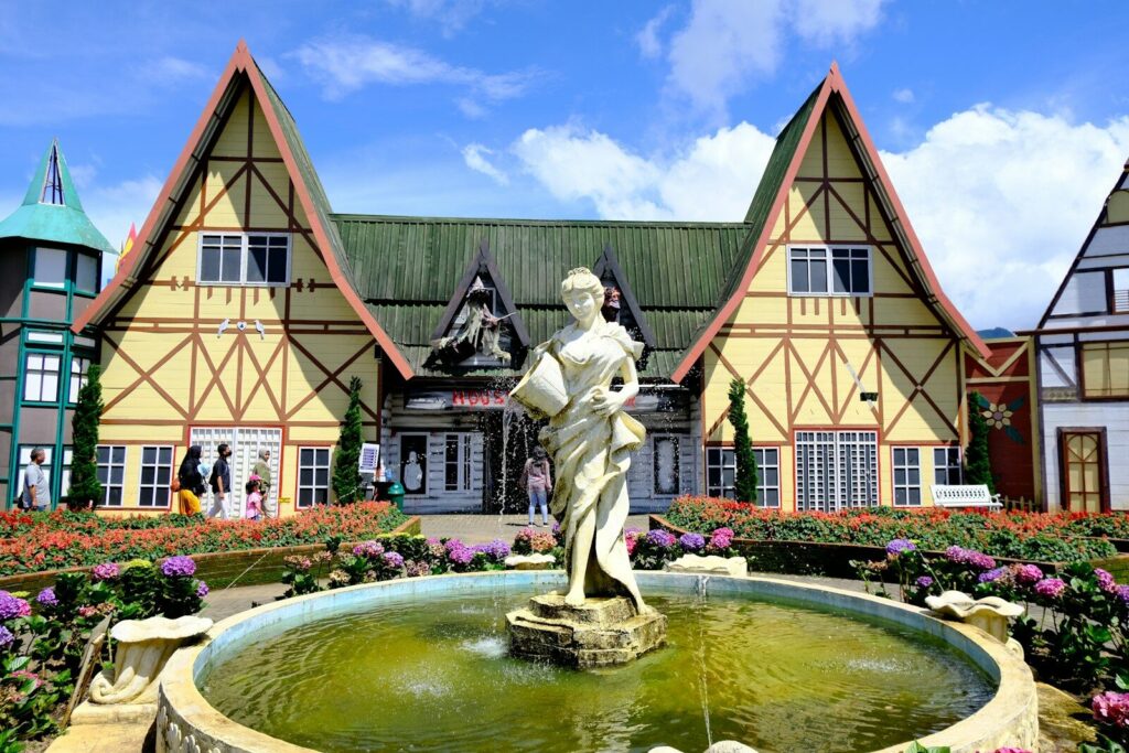 a fountain in front of a house with flowers around it