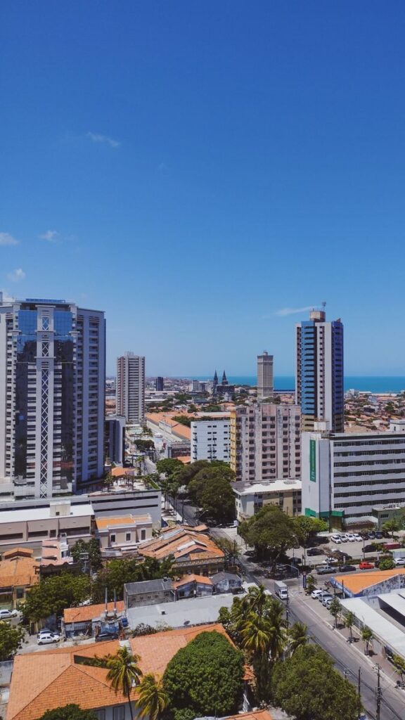 Aerial view of a modern city skyline with high-rise buildings and ocean backdrop, under clear blue skies.