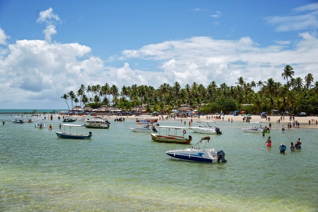 A vibrant tropical beach scene with boats and tourists under a clear blue sky.