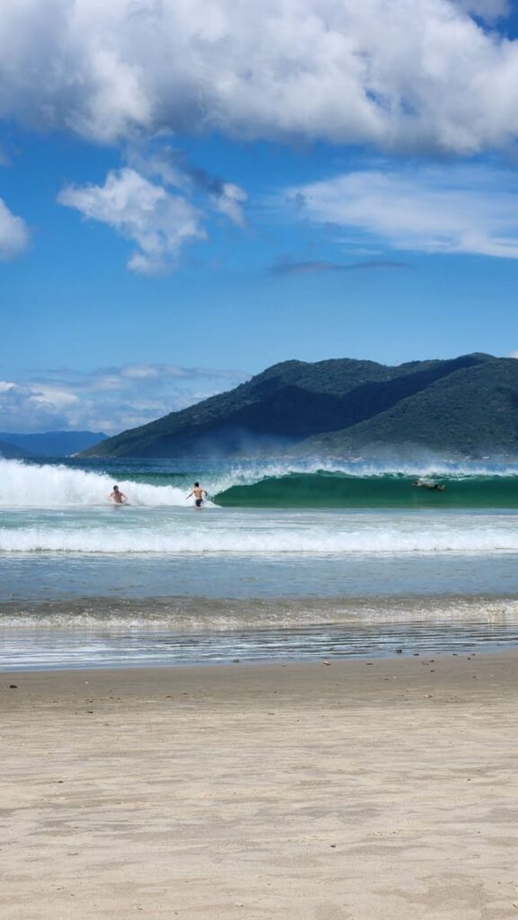 Surfing enthusiasts catch waves at a stunning Florianópolis beach with scenic mountain views.