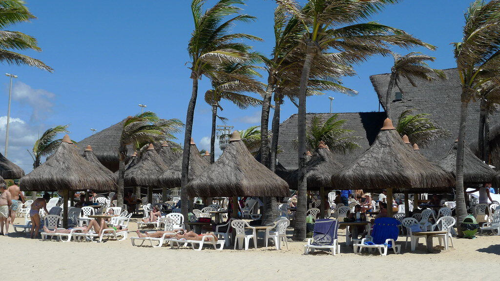 Praia tropical, coqueiros, barracas, pessoas
