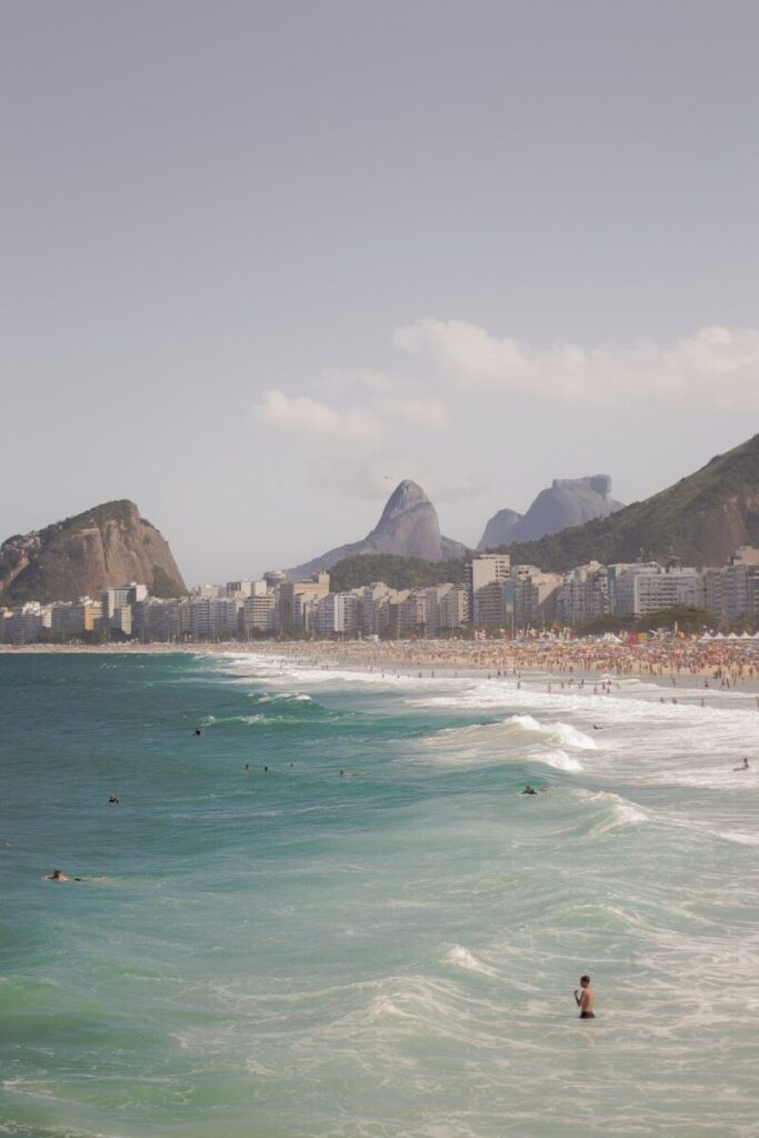 a beach with people in the water and mountains in the background
